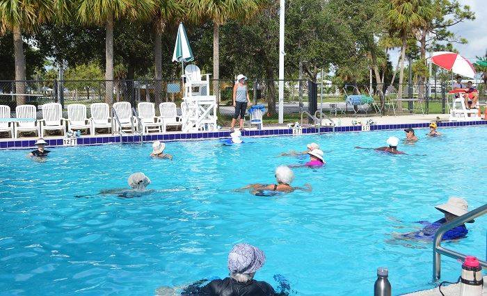 A group of women in the water doing water aerobics with the instructor on deck.